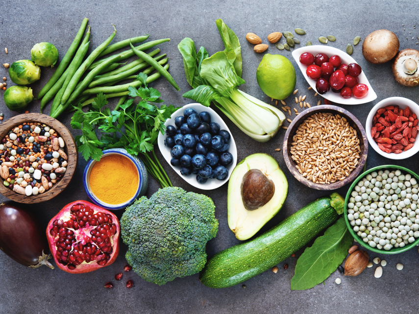 Healthy and nutritious food including beans, fruits, vegetables, and legumes are artfully displayed on a stone gray surface